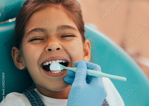 Cute little girl getting teeth exam at dental clinic photo
