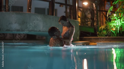 Couple of man and woman swimming in a swimming pool at night. Couple male and female swimming in the pool together at night