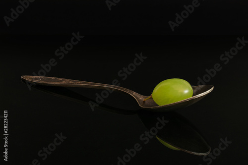 One whole fresh green grape with antique spoon isolated on black glass