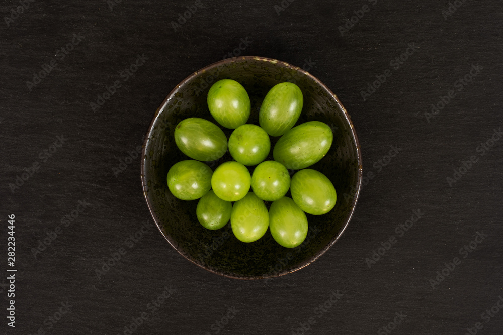 Lot of whole fresh green grape in dark ceramic bowl flatlay on grey stone