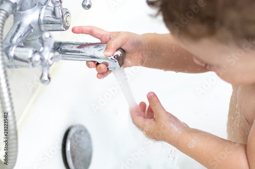 child washes in the bath, baby girl boy plays with a stream of water