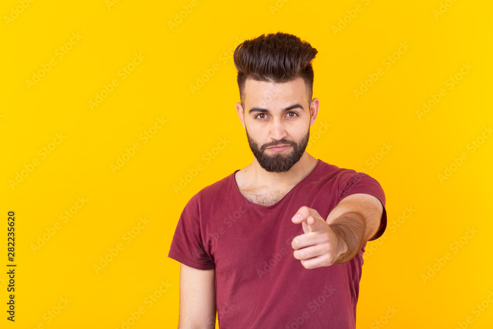 Cute young hipster man with a beard pointing at the camera is posing on a yellow background with copy space. Concept of choice and win. Cute young hipster man with a beard pointing at the camera is posing on a yellow background with copy space. Concept of choice and win.