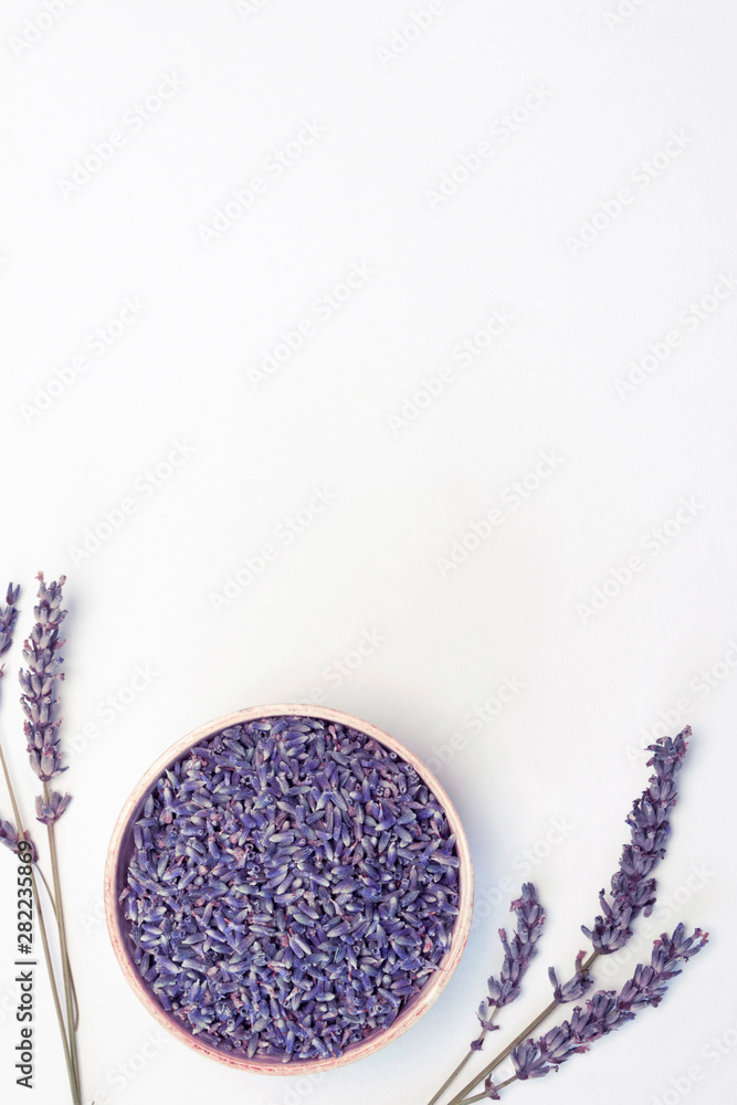 Fototapeta Lavender flowers in wooden plate and branches on white background, toned. Invitation, spa, recipe concept. Top view, close-up, flat lay, copy space, layout design, vertical format