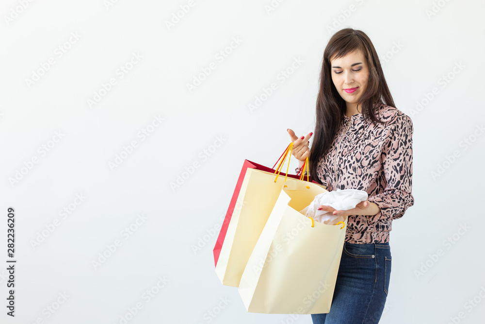 Positive young stylish brunette woman holding bags posing on a white background with copy space. Shopping concept in a mall. Positive young stylish brunette woman holding bags posing on a white background with copy space. Shopping concept in a mall.