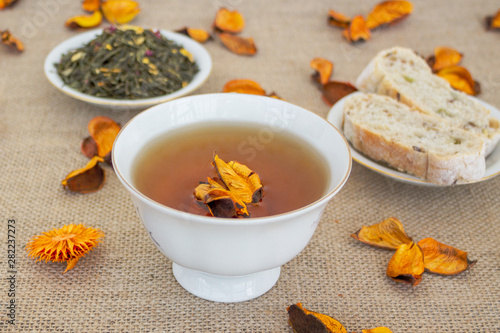 Herbal tea with grain bread and orange dried flowers on sackcloth background.