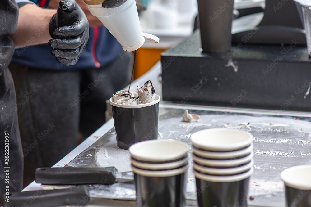 Seller of Ice Cream adding Topping as chocolate Syrup on sweet Dessert in paper Cup in Street Cafe Seller of Ice Cream adding Topping as chocolate Syrup on sweet Dessert in paper Cup in Street Cafe