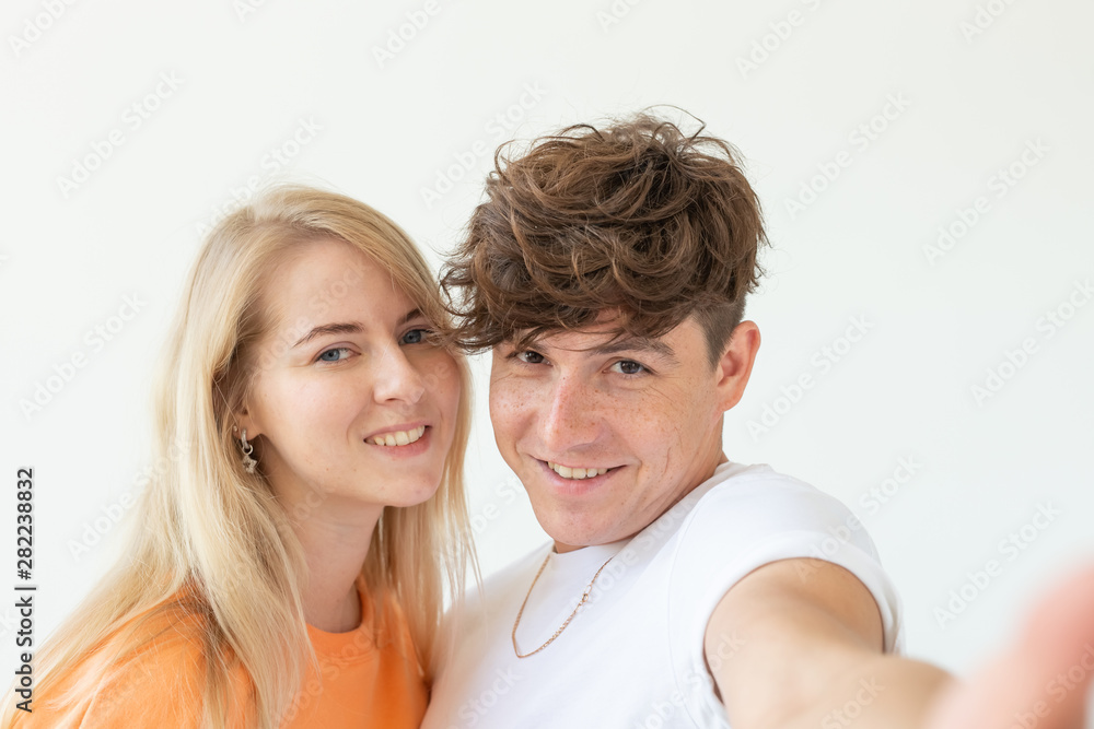 Charming young couple cute blond girl girl take a selfie posing over white background. Concept a young couple of teenagers or millennials In love. Charming young couple cute blond girl girl take a selfie posing over white background. Concept a young couple of teenagers or millennials In love.