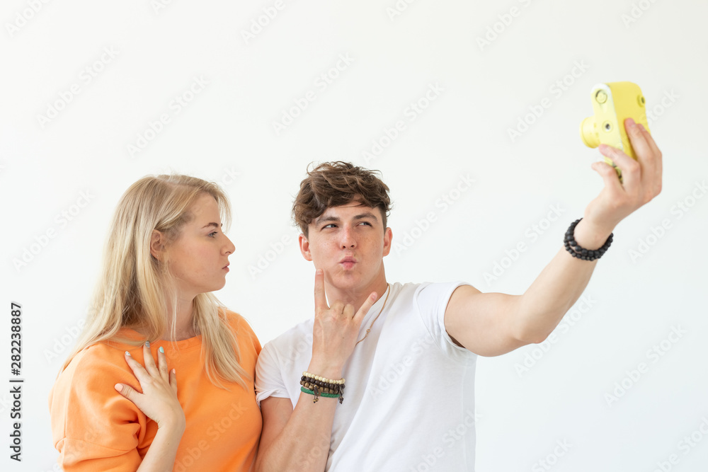 Funny young couple in love cute man and charming woman making selfie on vintage yellow film camera posing on a white background. Concept lovers of photography and hobbies.