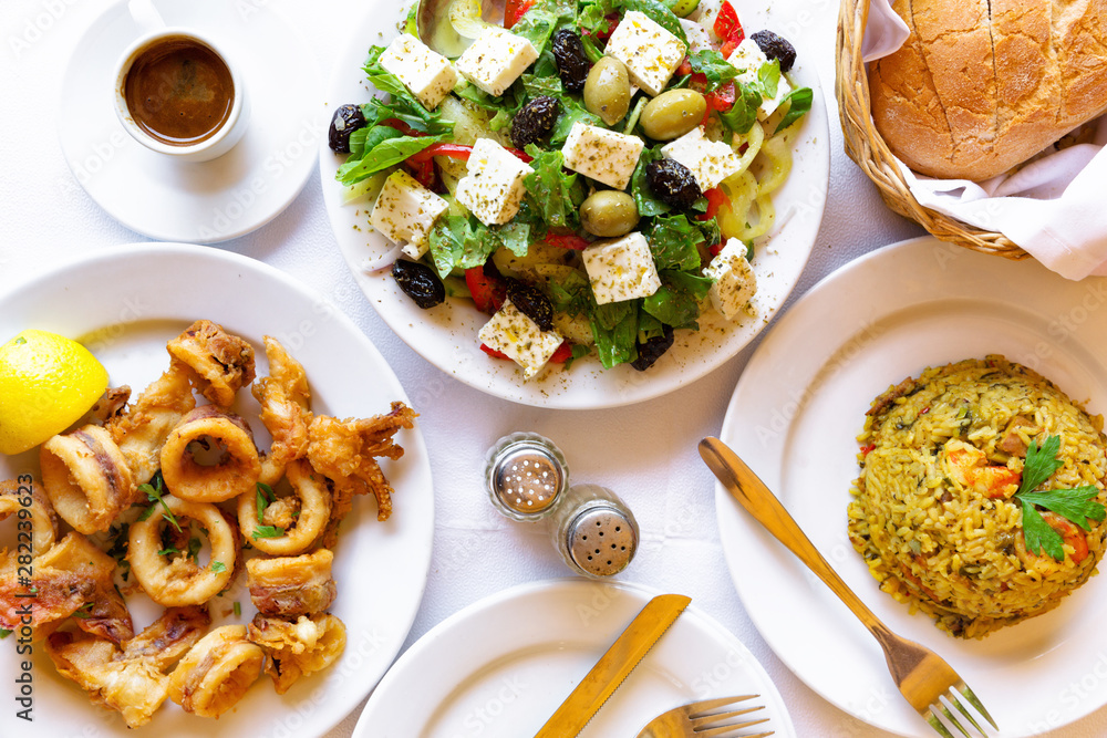 Top view of restaurant served seafood dishes. Fried squids, seafood risotto, greek salad, bread and greek coffee. Top view of restaurant served seafood dishes. Fried squids, seafood risotto, greek salad, bread and greek coffee.