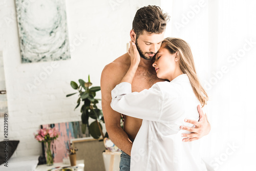 sexy young couple hugging each other with tender while standing near window