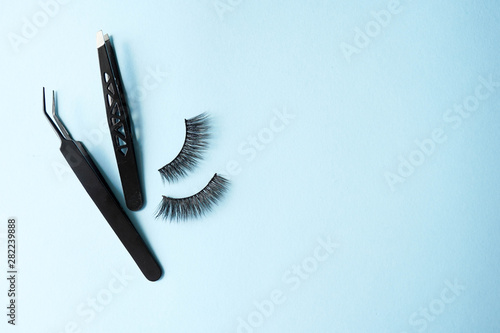 False eye lashes, black tweezers on blue background with copy space, mockup. Instruments: Beauty and fashion concept - Tools for eyelash extension.