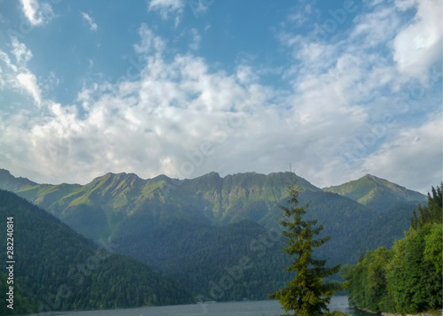 Mountain lake Ritsa in Abkhazia, green mountain tops, forest and blue sky with white clouds