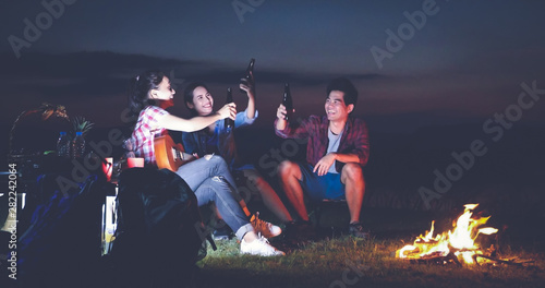 A group of Asian friends tourist drinking and playing guitar together with happiness in Summer while having camping near lake at sunset © tuiphotoengineer