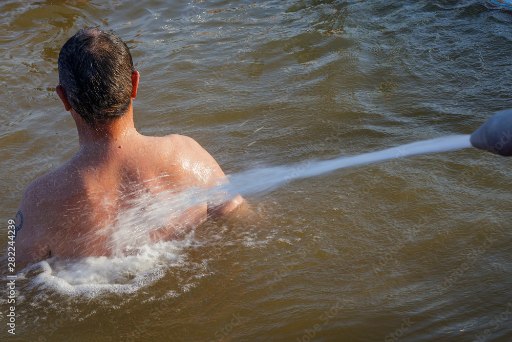 A man receives a back hydromassage with a powerful jet from the nozzle. A man receives a back hydromassage with a powerful jet from the nozzle.