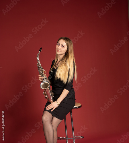 Beautiful european girl holds saxaphone in hand on burgundy background