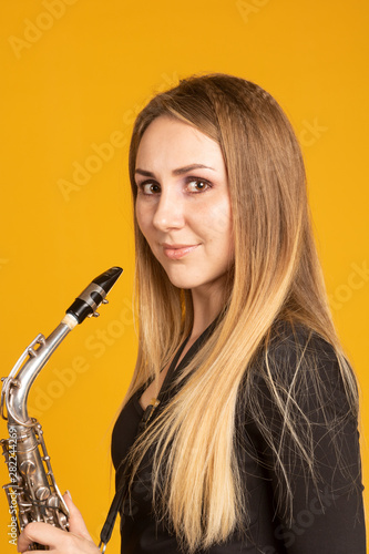 Beautiful european girl holds saxophone on yellow background