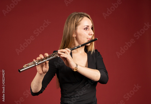 Beautiful European girl plays the flute on a burgundy background