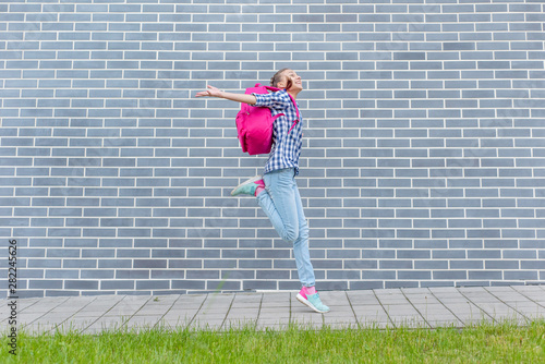 Happy schoolchild with backpack run to school on street next to an Brick Wall. Cheerful cute child pupil Teen Girl Back to School. Concepts of freedom, childhood and education.