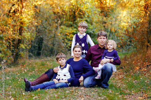 Portrait of young parents with three children. Mother, father, two kids brothers boys and little cute toddler sister girl having fun together in autumn forest. Happy family of five