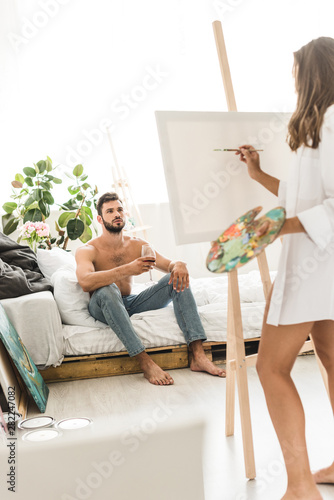 selective focus of man sitting in bed with wine and girl drawing guy
