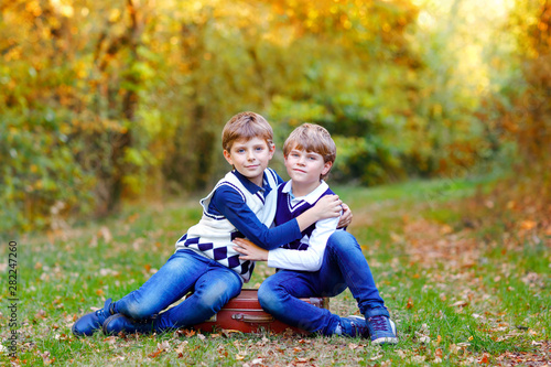 Portrait of little school kids boys sitting in forest. Happy children, best friends and siblings having fun on warm sunny day early autumn. Twins and family, nature and active leisure.