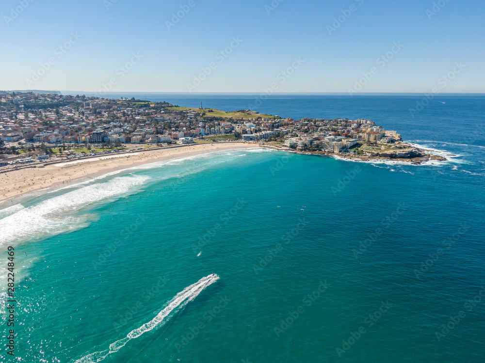 Beautiful aerial high angle drone view of the suburbs of Bondi Beach and North Bondi, one of the most famous beaches in Sydney, New South Wales, Australia. Motor boat driving through the ocean.