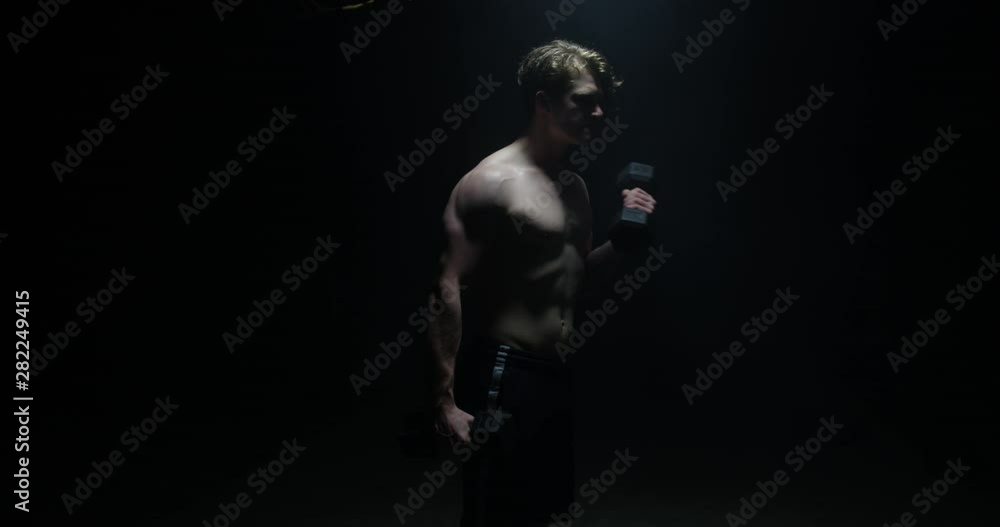 Close Up Portrait Of Man Lifting Weights Looking Away From Camera On Spotlight Preparing For Big Match Wearing White T-shirt Close Up Portrait Of Man Lifting Weights Looking Away From Camera On Spotlight Preparing For Big Match Wearing White T-shirt