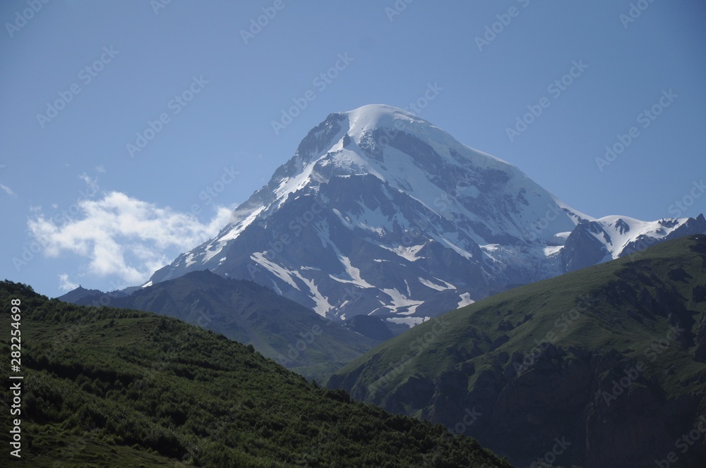 The Kazbek peak among the other Caucasus mountains that have come up against the blue sky
