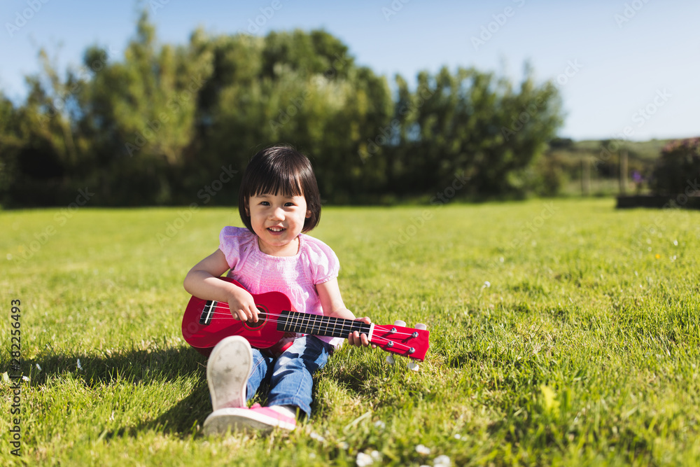 Fototapeta premium toddler girl playing guitar at sunny countryside home garden