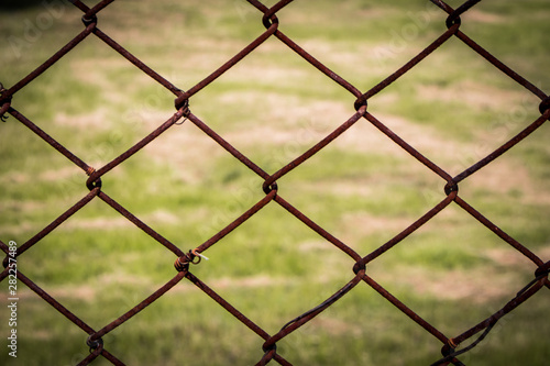 The close up of brown wire fence (barricade) which is hardly rusted in blurred background (meadow).