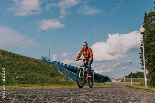 A man in jeans and a red shirt rides a bicycle on the road. The concept of an active lifestyle. Place for text.
