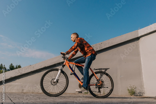 A man in jeans and a red shirt rides a bicycle on the road. The concept of an active lifestyle. Place for text.