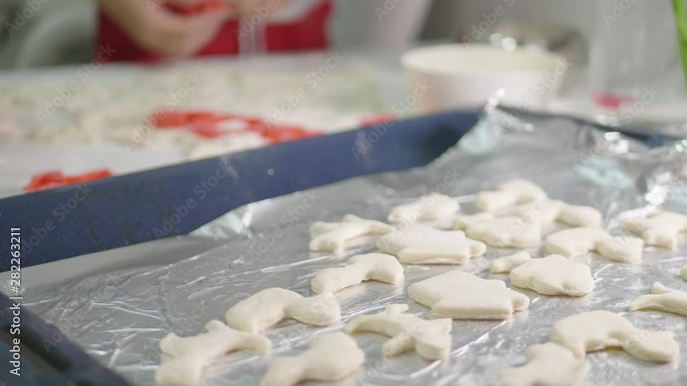 Little child girl helping her mother in the kitchen to make cookies. Making different shapes of cookies on the kitchen desk. Homemade cookies close up. Little child girl helping her mother in the kitchen to make cookies. Making different shapes of cookies on the kitchen desk. Homemade cookies close up.