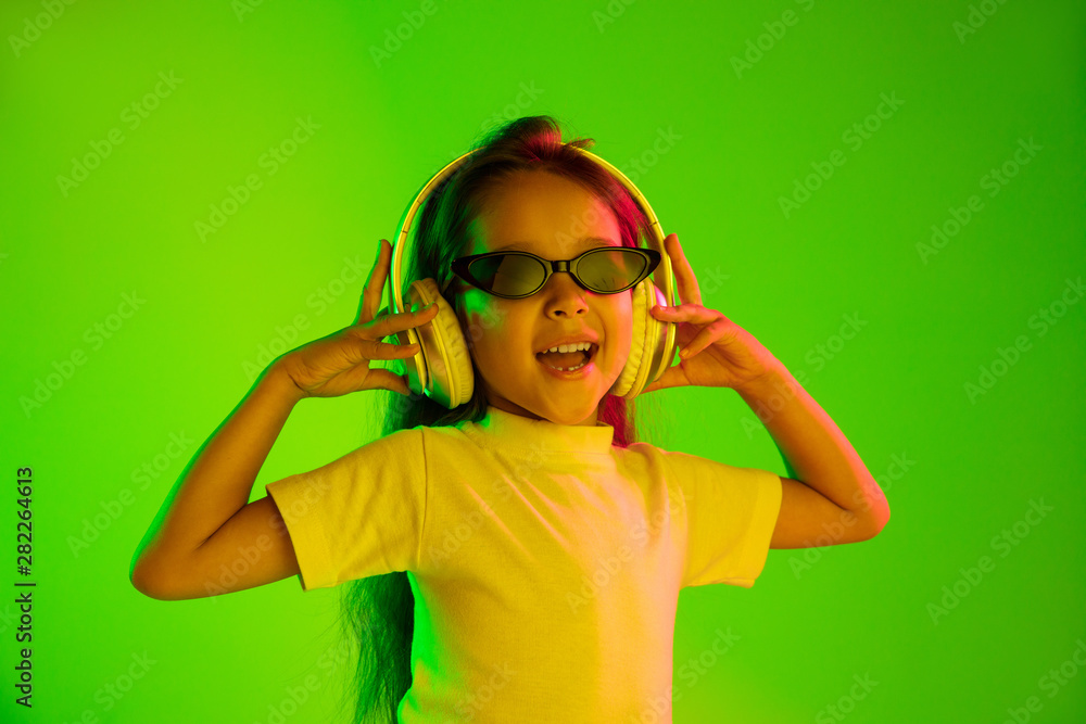 Beautiful female half-length portrait isolated on green backgroud in neon light. Young emotional teen girl in sunglasses. Human emotions, facial expression concept. Trendy colors. Dancing, smiling. Beautiful female half-length portrait isolated on green backgroud in neon light. Young emotional teen girl in sunglasses. Human emotions, facial expression concept. Trendy colors. Dancing, smiling.