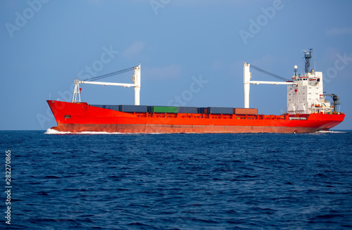 Bright red-white container ship in the sea. Blue ocean waves and sky. Transportation of containerized cargo ship by sea.