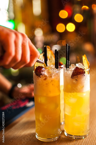 Close-up of expert bartender making three orange cocktail with dried orange in bar