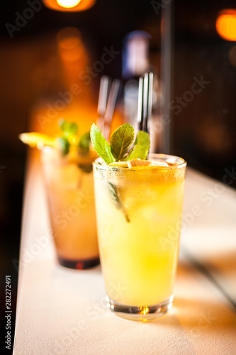 Two orange cocktails with orange and mint on the bar, blurred background.