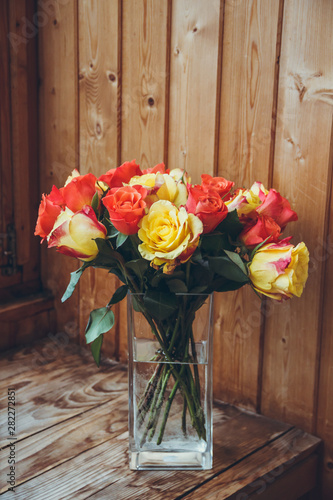 Bouquet of roses in a vase on a wooden background. Flowers in a vase. Orange and yellow flowers in a vase. Transparent vase.