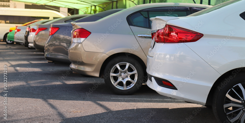 Closeup of rear, back side of white car with  other cars parking in outdoor parking lot in sunny day. 