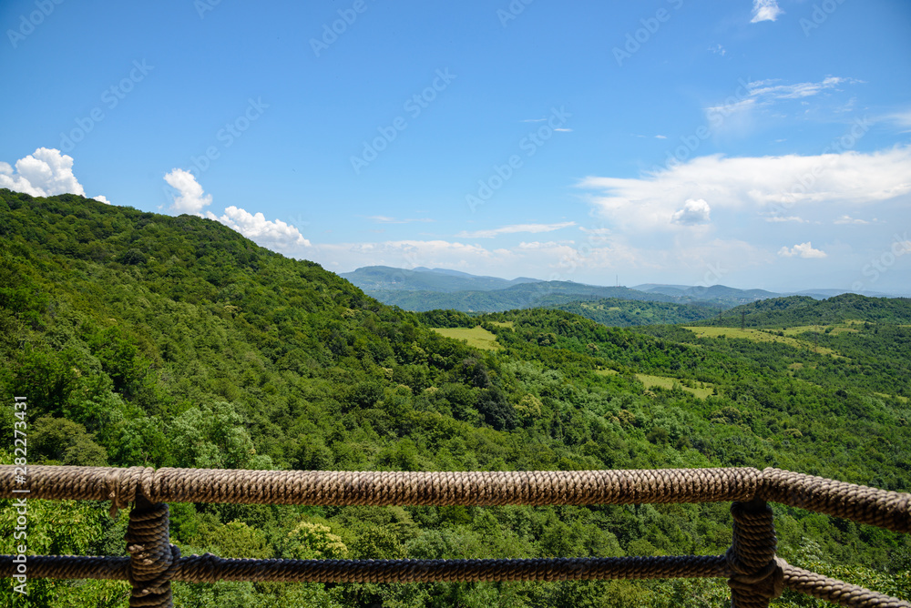 view of the mountain green valley surrounded by dense vegetation of green trees on a sunny day with clouds in the sky, from the observation deck.