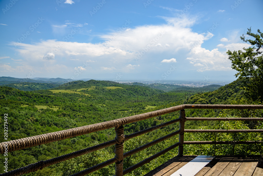 view of the mountain green valley surrounded by dense vegetation of green trees on a sunny day with clouds in the sky, from the observation deck.