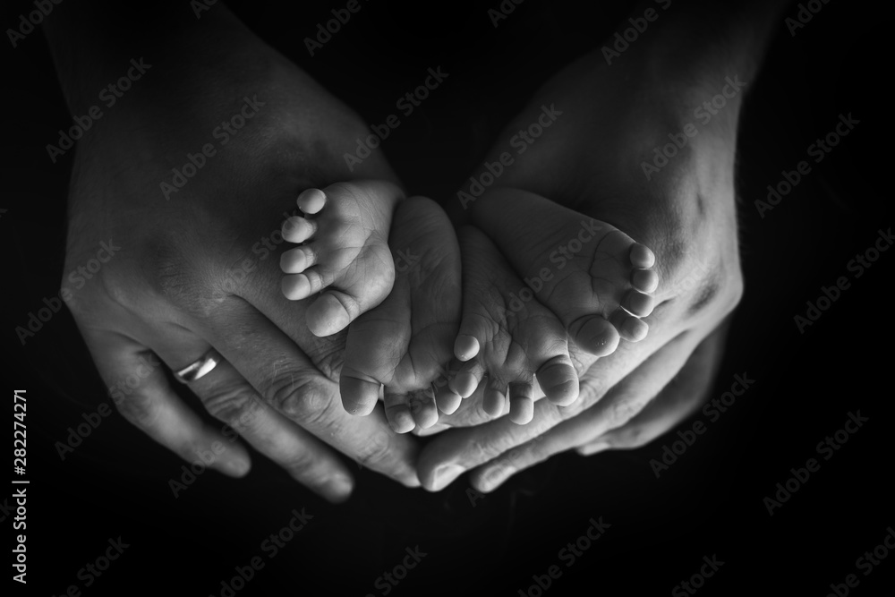 Fototapeta premium Little foot of a newborn baby on a black background close-up
