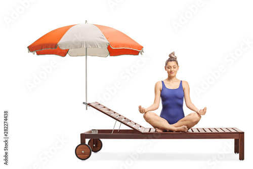Young woman in a swimming suit meditating on a sunbed under umbrella