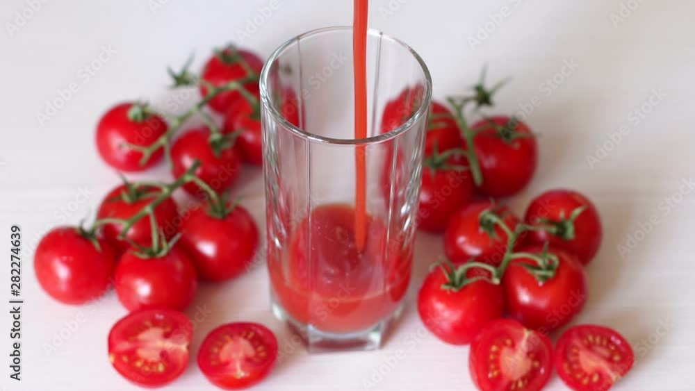 Close-up pour tomato juice into an empty glass, lie next to fresh cherry tomatoes. White background. Slow motion. The view from the top. Close-up pour tomato juice into an empty glass, lie next to fresh cherry tomatoes. White background. Slow motion. The view from the top.