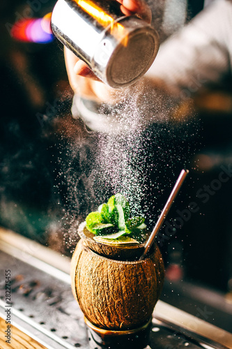 Bartender finishes preparation of exotic alcoholic cocktail in coconut by adding a bitter of powdered sugar. Close-up of expert bartender making cocktail in bar. photo