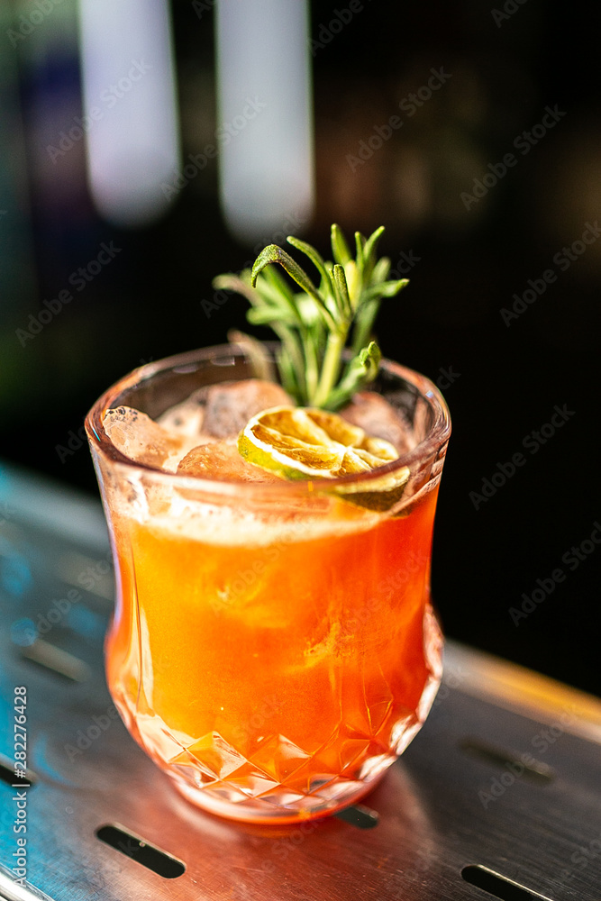 Close-up orange cocktail with dried lemon and rosemary on the bar, blurred background. Close-up orange cocktail with dried lemon and rosemary on the bar, blurred background.