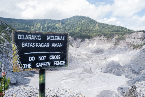 View of the warning sign “Do not cross the safety fence” in English, as same as “Dilarang Melewati Batas Pagar Aman” in Indonesian language at Tangkuban Perahu volcano in Bandung, Indonesia. photo