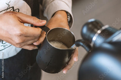 barista is steaming milk with making latte art coffee. soft-focus and over light in the background