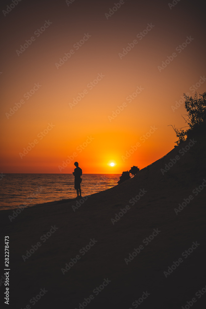 Silhouettes of a Man in front of a breathtaking sunset at the seaside