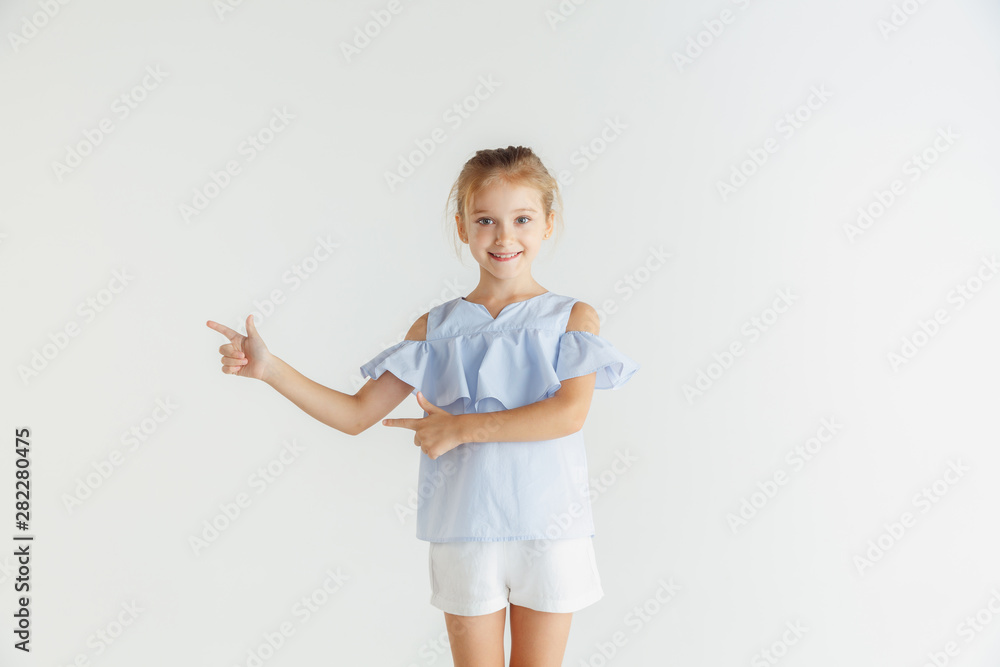 Stylish little smiling girl posing in casual clothes isolated on white studio background. Caucasian blonde female model. Human emotions, facial expression, childhood. Pointing on empty space bar. Stylish little smiling girl posing in casual clothes isolated on white studio background. Caucasian blonde female model. Human emotions, facial expression, childhood. Pointing on empty space bar.
